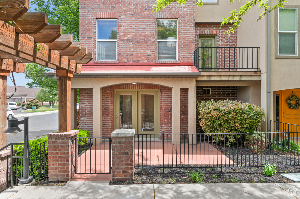 Doorway to property with fence, stucco siding, brick siding, a balcony, and a porch