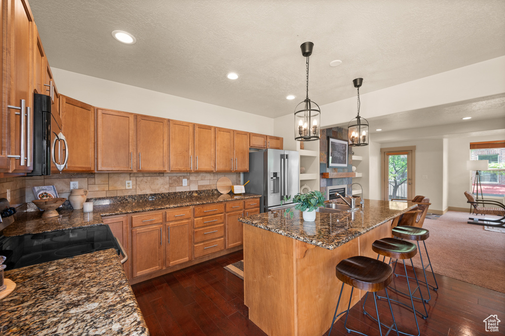 Kitchen featuring stainless steel appliances, brown cabinets, a sink, decorative backsplash, and dark wood-type flooring