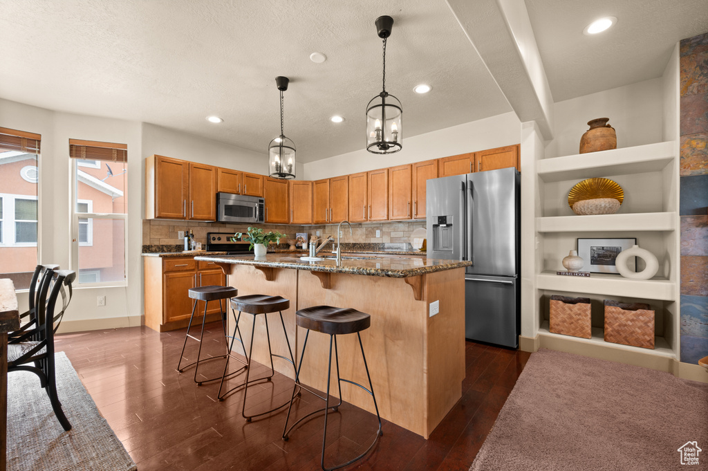 Kitchen with appliances with stainless steel finishes, backsplash, a breakfast bar area, dark wood finished floors, and recessed lighting