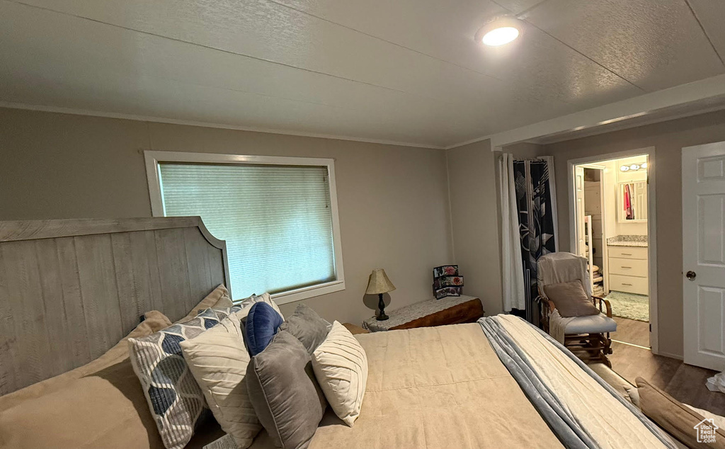 Bedroom featuring wood finished floors, ornamental molding, and ensuite bathroom