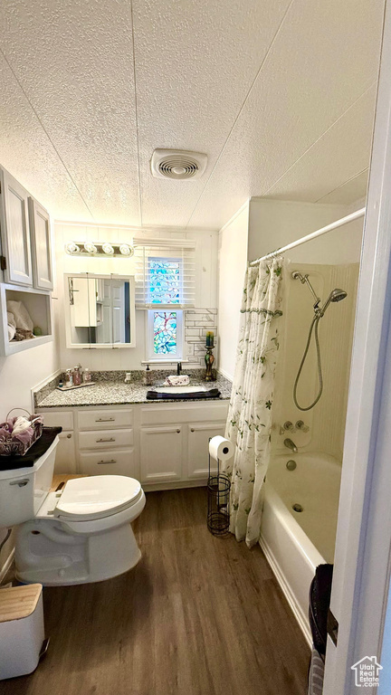 Full bathroom with a textured ceiling, wood finished floors, toilet, shower / tub combo, and vanity