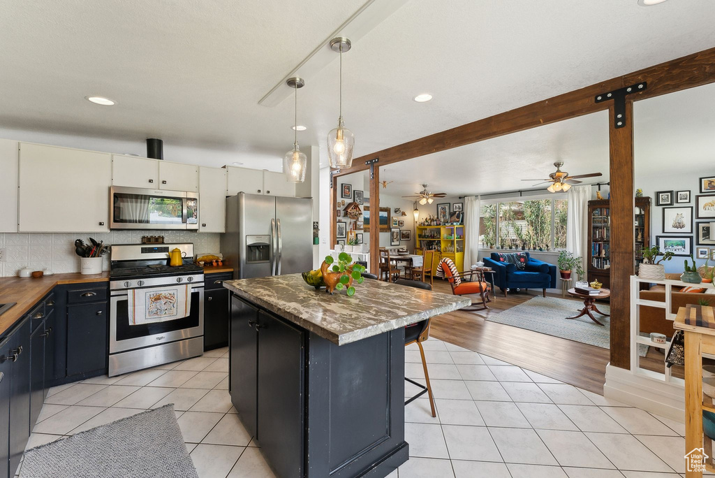 Kitchen featuring appliances with stainless steel finishes, a kitchen island, light tile patterned floors, ceiling fan, and open floor plan
