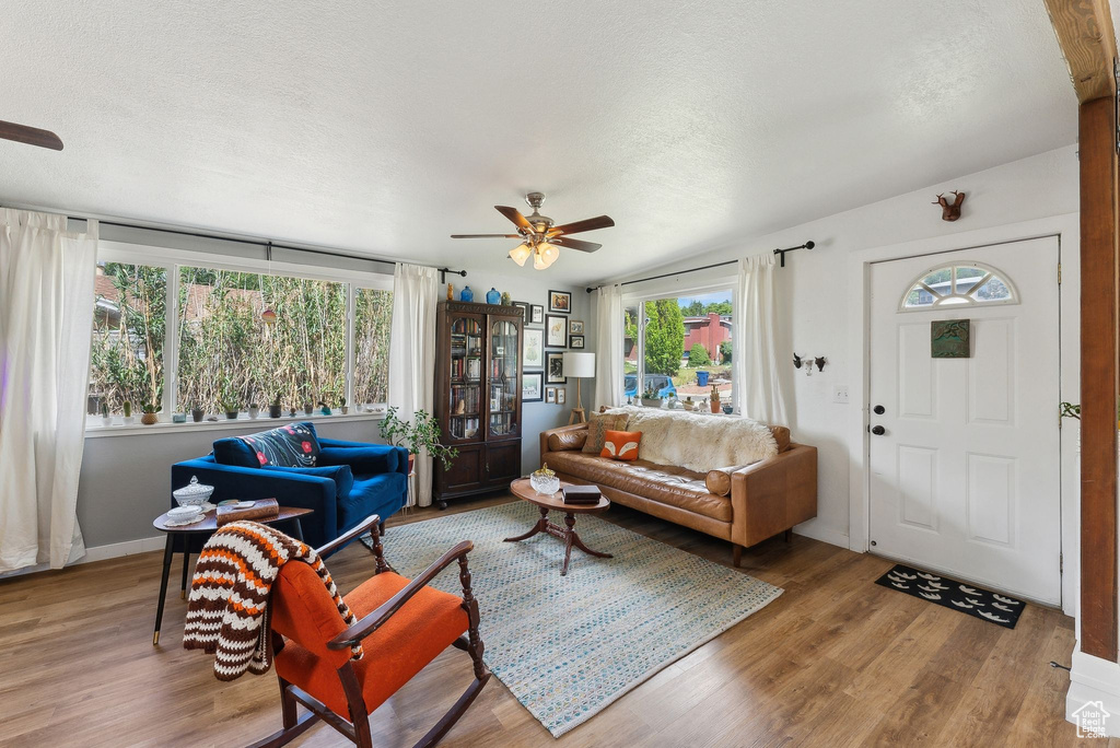 Living room with ceiling fan, plenty of natural light, wood finished floors, and a textured ceiling