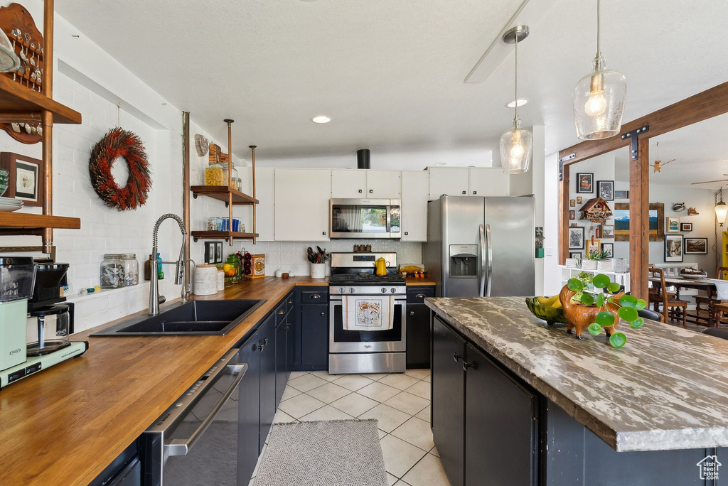 Kitchen featuring appliances with stainless steel finishes, wood counters, a sink, open shelves, and light tile patterned floors