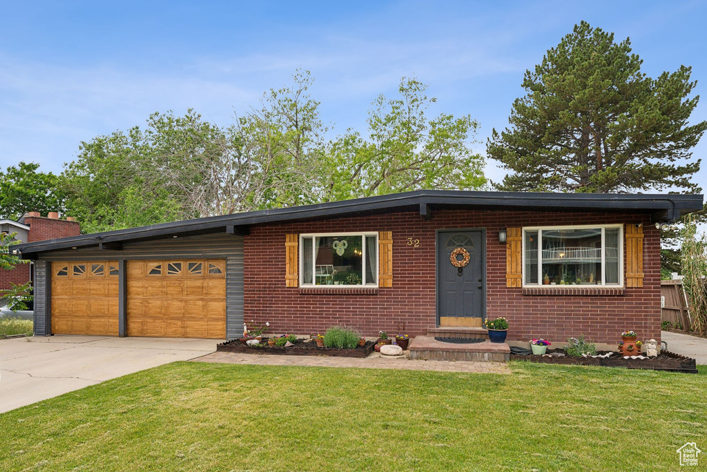 View of front of home with a front lawn, driveway, brick siding, and a garage
