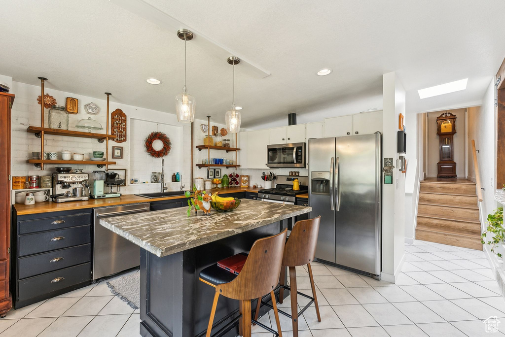 Kitchen featuring stainless steel appliances, open shelves, a breakfast bar, light tile patterned floors, and a center island