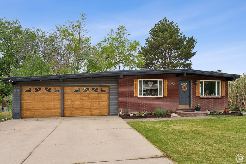 View of front facade with driveway, a garage, a front lawn, and brick siding