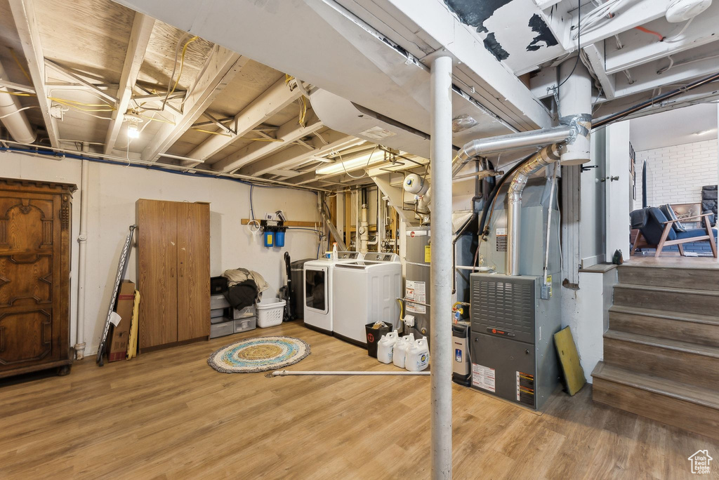 Unfinished basement with washer and dryer, wood finished floors, heating unit, gas meter, and stairs