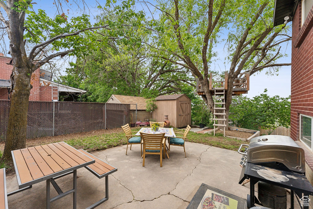 View of patio with outdoor dining area, a storage unit, a fenced backyard, an outdoor structure, and stairway