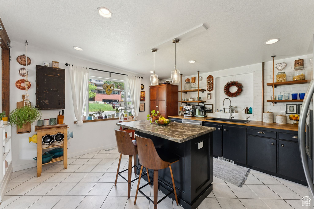 Kitchen with open shelves, a sink, a kitchen island, light tile patterned floors, and a kitchen bar