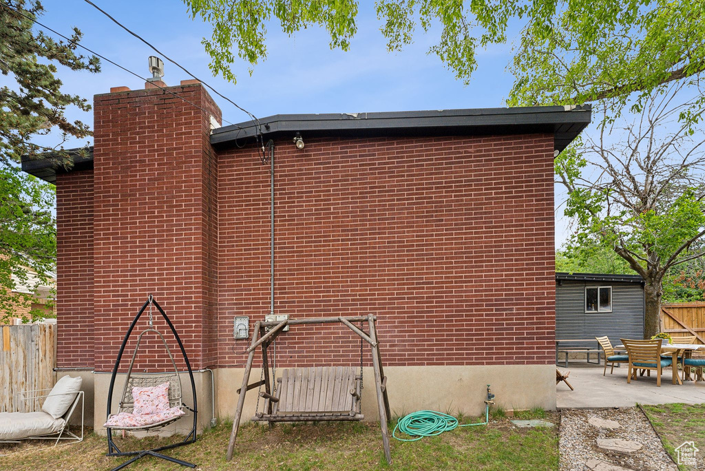 View of side of home with fence, a patio, brick siding, and a chimney