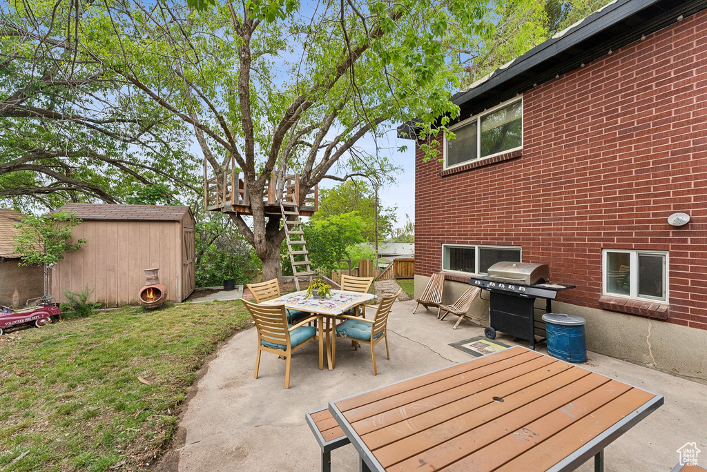 View of patio with outdoor dining area, a storage unit, an outbuilding, a grill, and fence