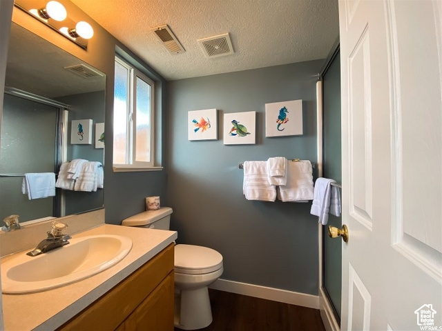Bathroom featuring a shower stall, vanity, wood finished floors, toilet, and baseboards