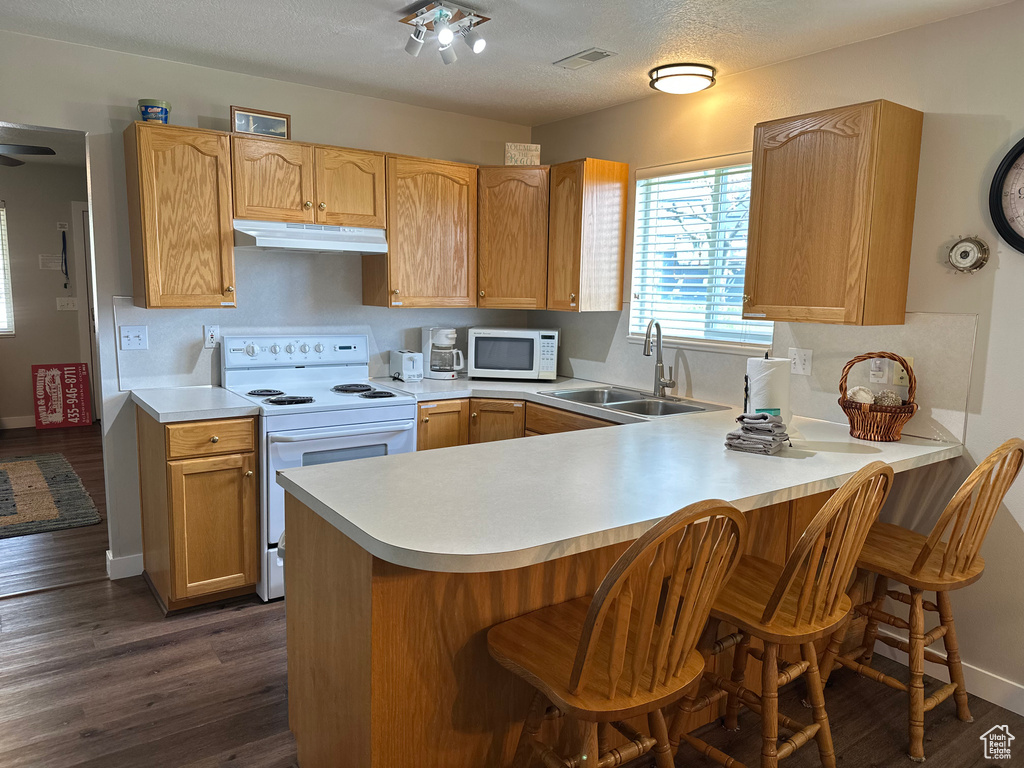Kitchen featuring white appliances, under cabinet range hood, a sink, light countertops, and a textured ceiling