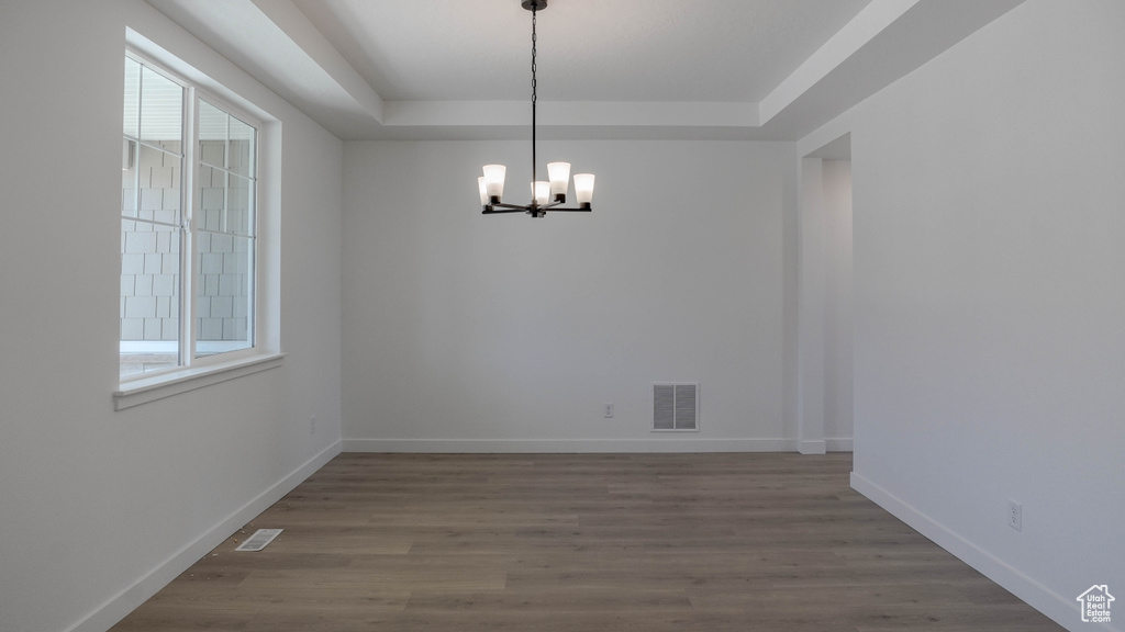 Spare room with a chandelier, a raised ceiling, and wood finished floors