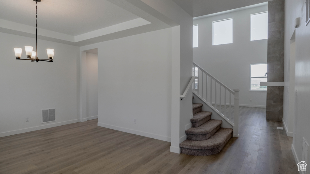 Staircase with a chandelier, wood finished floors, and a raised ceiling