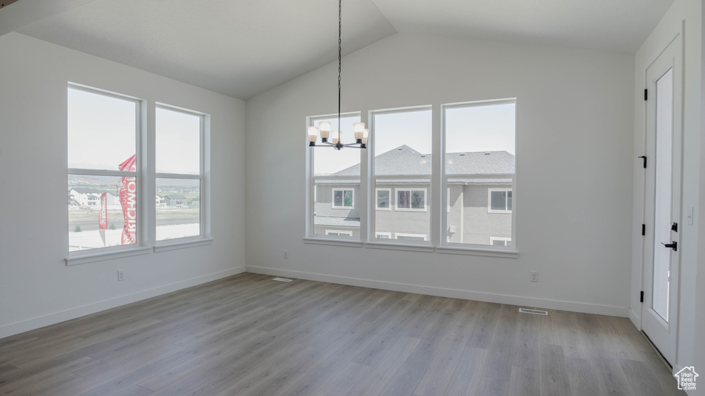 Unfurnished dining area with a chandelier, vaulted ceiling, and light wood finished floors
