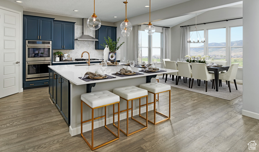 Kitchen featuring stainless steel double oven, wall chimney range hood, blue cabinetry, a chandelier, and a mountain view