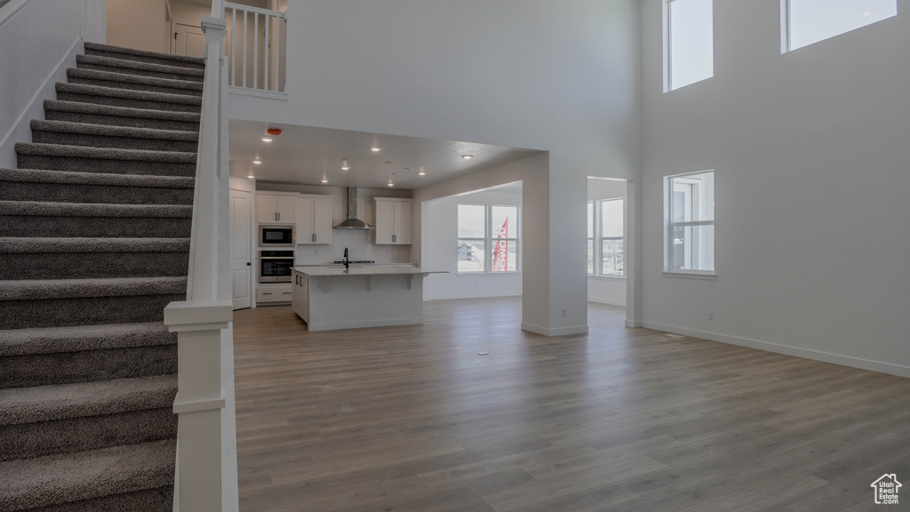 Unfurnished living room featuring stairway, plenty of natural light, a towering ceiling, and light wood-style floors