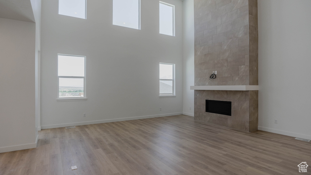 Unfurnished living room featuring a high ceiling, light wood finished floors, and a tile fireplace
