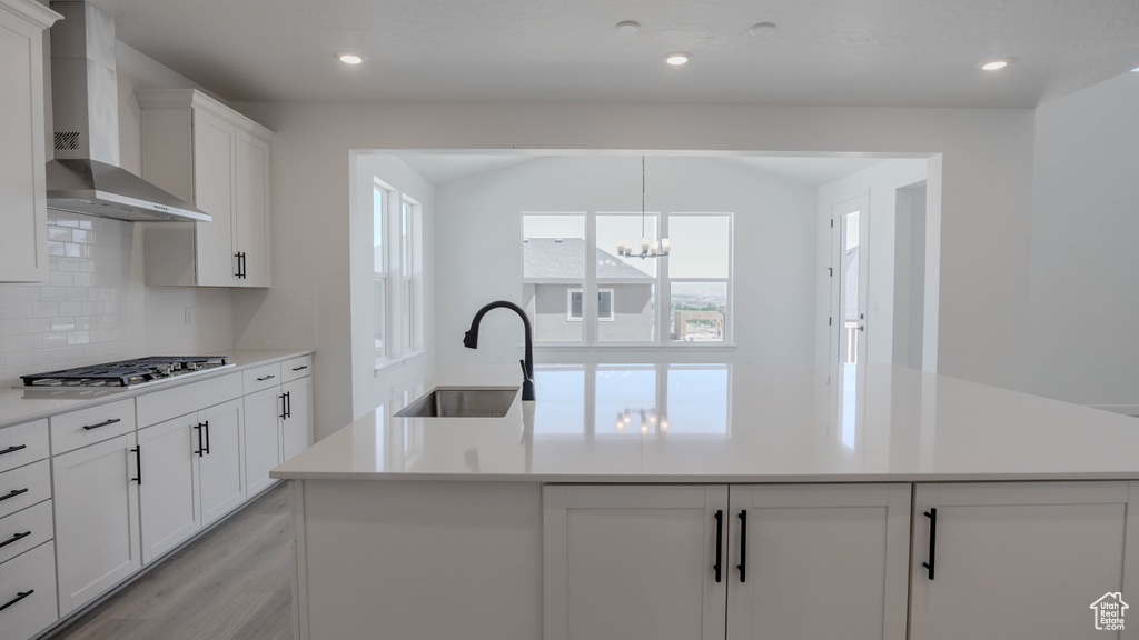 Kitchen featuring wall chimney range hood, healthy amount of natural light, decorative backsplash, stainless steel gas cooktop, and vaulted ceiling