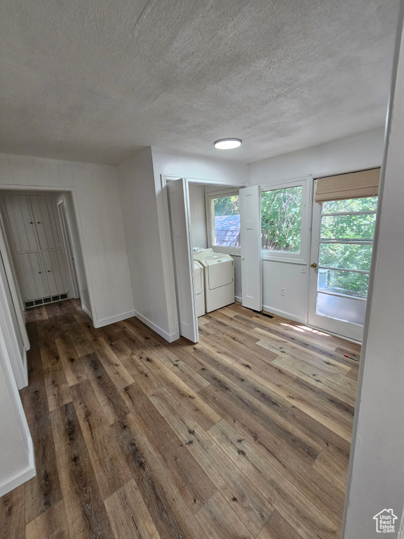 Unfurnished room featuring washing machine and dryer, hardwood / wood-style flooring, a textured ceiling, and baseboards