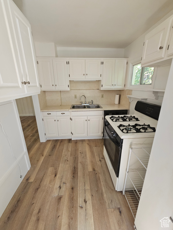 Kitchen featuring a sink, gas range, light countertops, and white cabinets