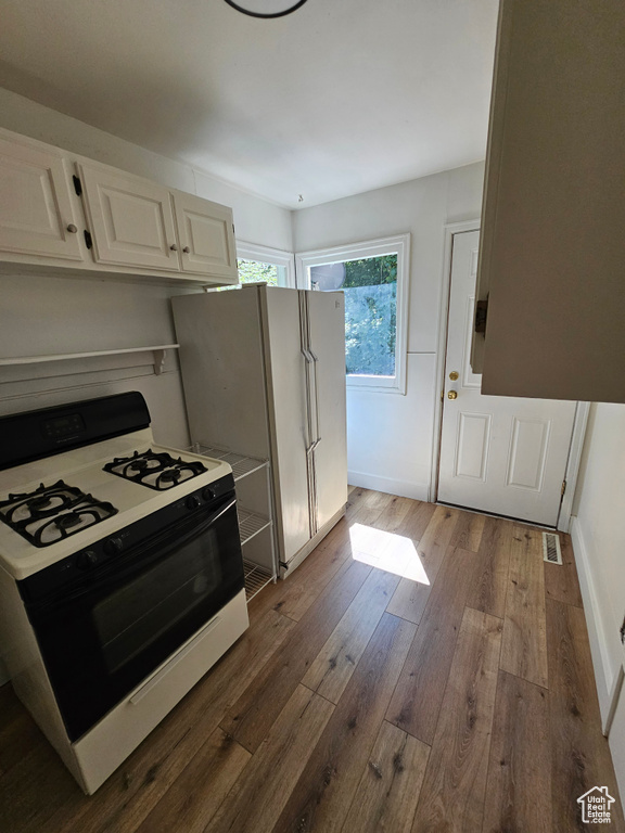 Kitchen featuring gas stove, white cabinets, dark wood-type flooring, freestanding refrigerator, and baseboards