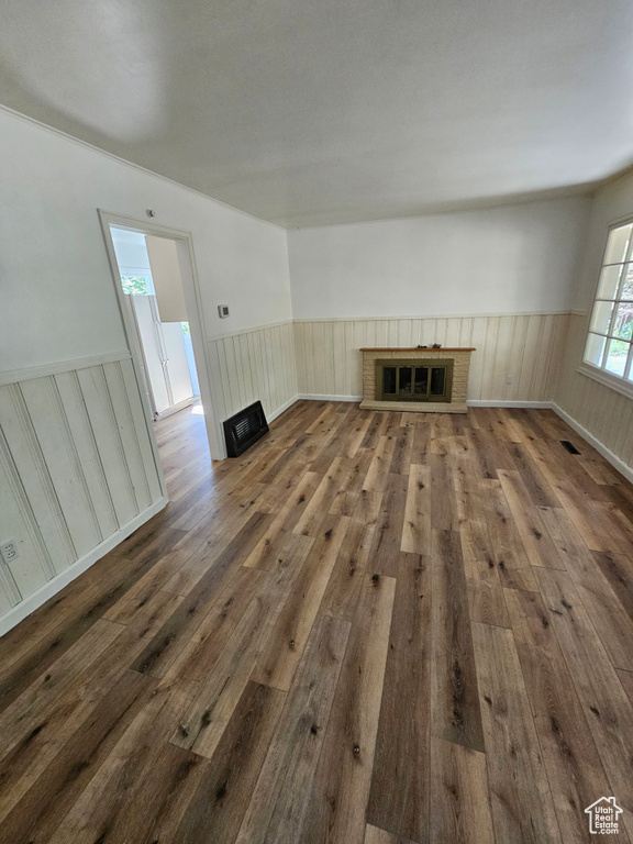 Unfurnished living room featuring a brick fireplace, wood-type flooring, and a wainscoted wall