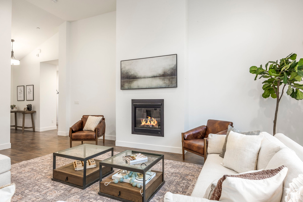 Living room with a glass covered fireplace, wood finished floors, baseboards, and high vaulted ceiling