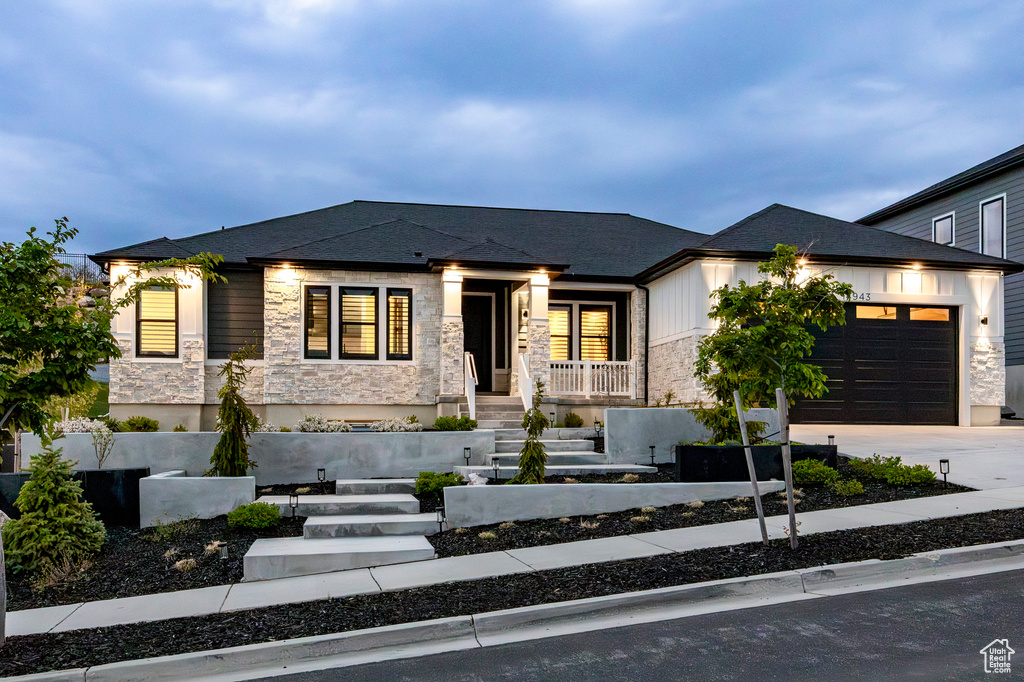 View of front of house with stone siding, an attached garage, driveway, and a porch