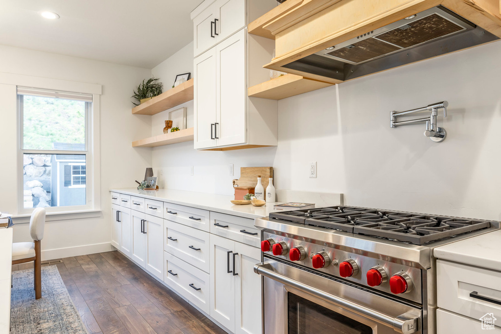 Kitchen with open shelves, custom exhaust hood, stainless steel range, light countertops, and dark wood finished floors