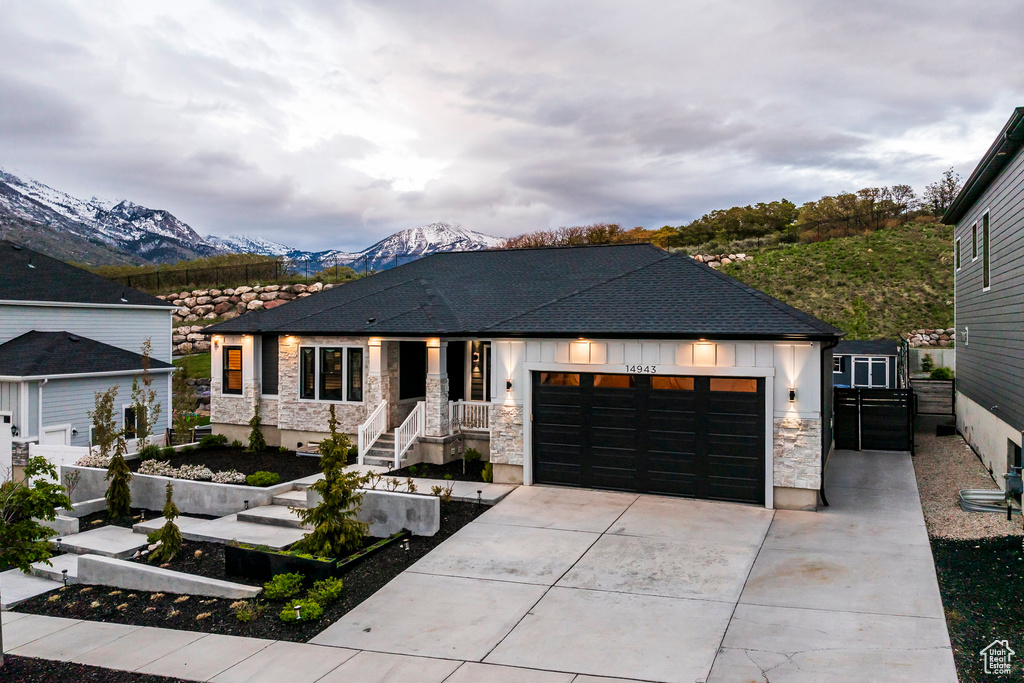 View of front of home featuring a garage, a mountain view, concrete driveway, stone siding, and fence