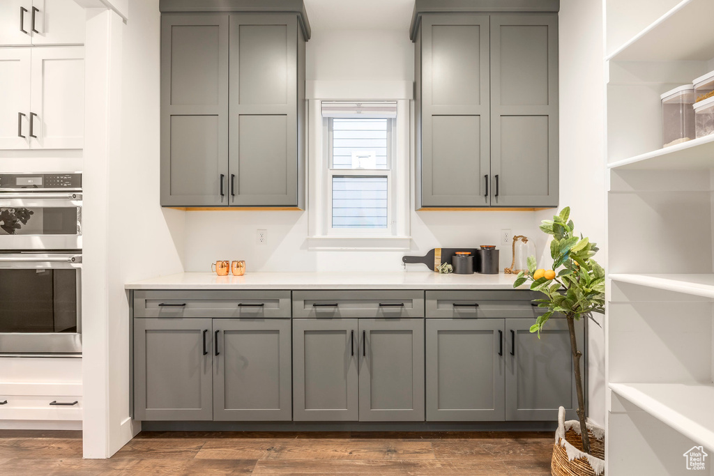 Kitchen featuring gray cabinetry, double oven, light countertops, open shelves, and wood finished floors