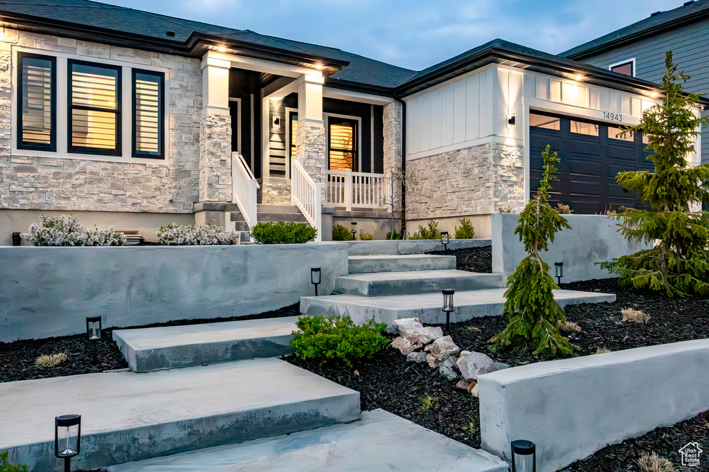 View of front of home featuring stone siding, a porch, and an attached garage