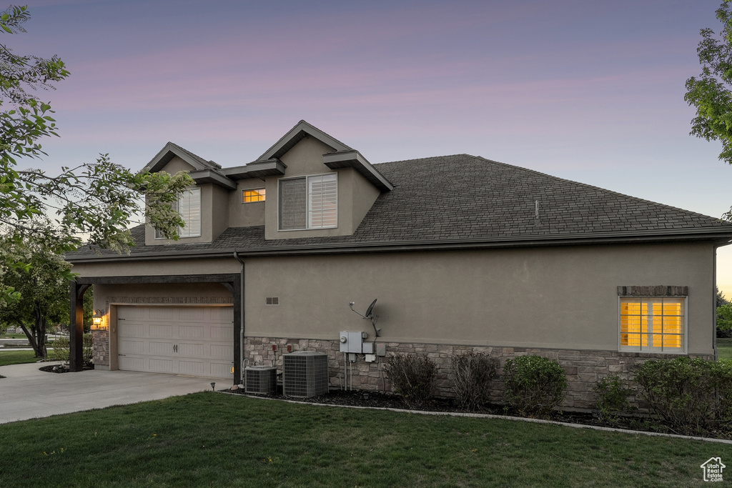 View of side of home with stucco siding, stone siding, driveway, central AC unit, and a yard