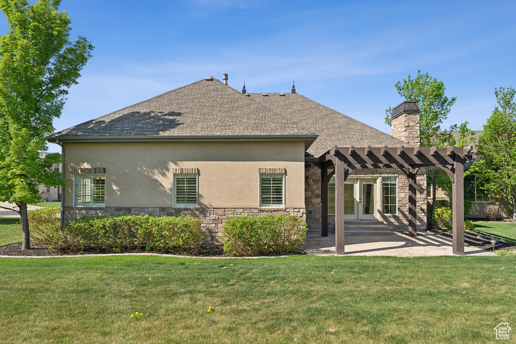 Back of house with a pergola, stone siding, stucco siding, and a yard