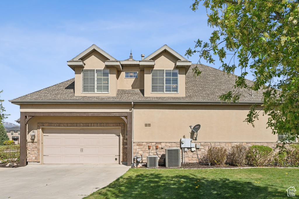 View of front of home featuring stucco siding, driveway, stone siding, cooling unit, and a front lawn