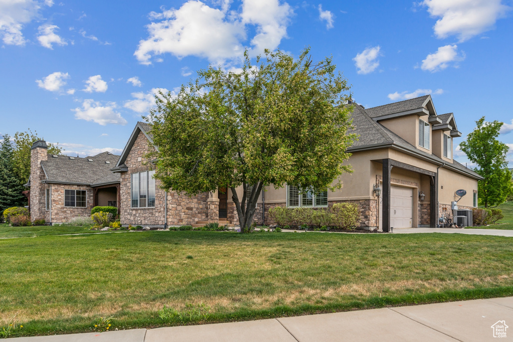 View of front of property with stucco siding, stone siding, concrete driveway, a front lawn, and a garage