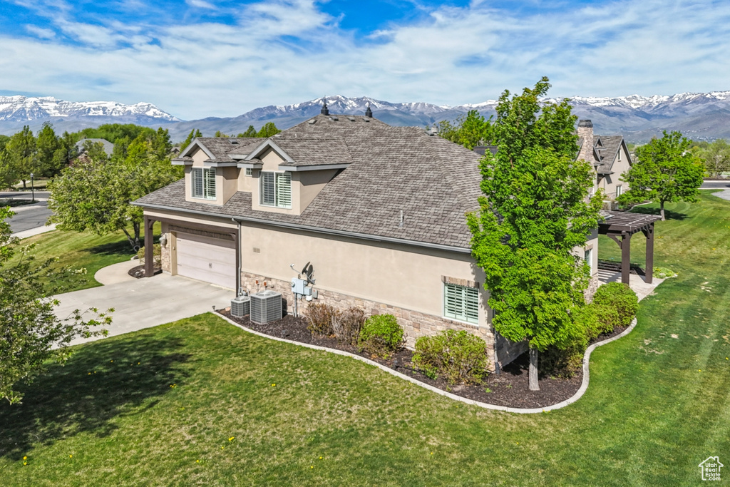 View of side of home with stucco siding, stone siding, concrete driveway, a mountain view, and a yard