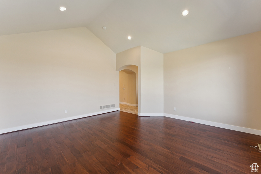 Empty room with arched walkways, recessed lighting, baseboards, dark wood finished floors, and vaulted ceiling