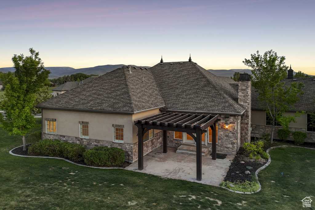 Rear view of house with a pergola, stucco siding, stone siding, a yard, and a patio area