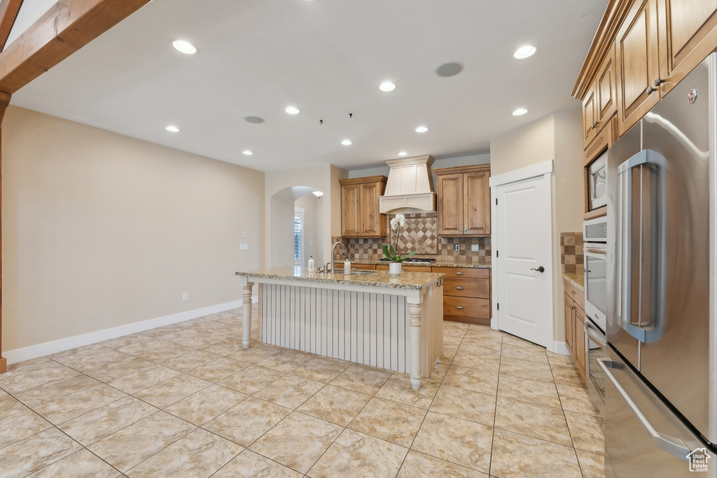 Kitchen featuring appliances with stainless steel finishes, premium range hood, arched walkways, a sink, and tasteful backsplash