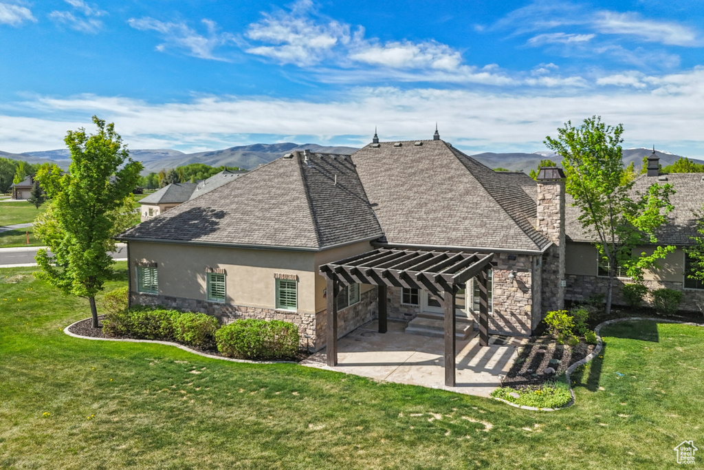 Rear view of property featuring stone siding, stucco siding, a pergola, a patio area, and a yard