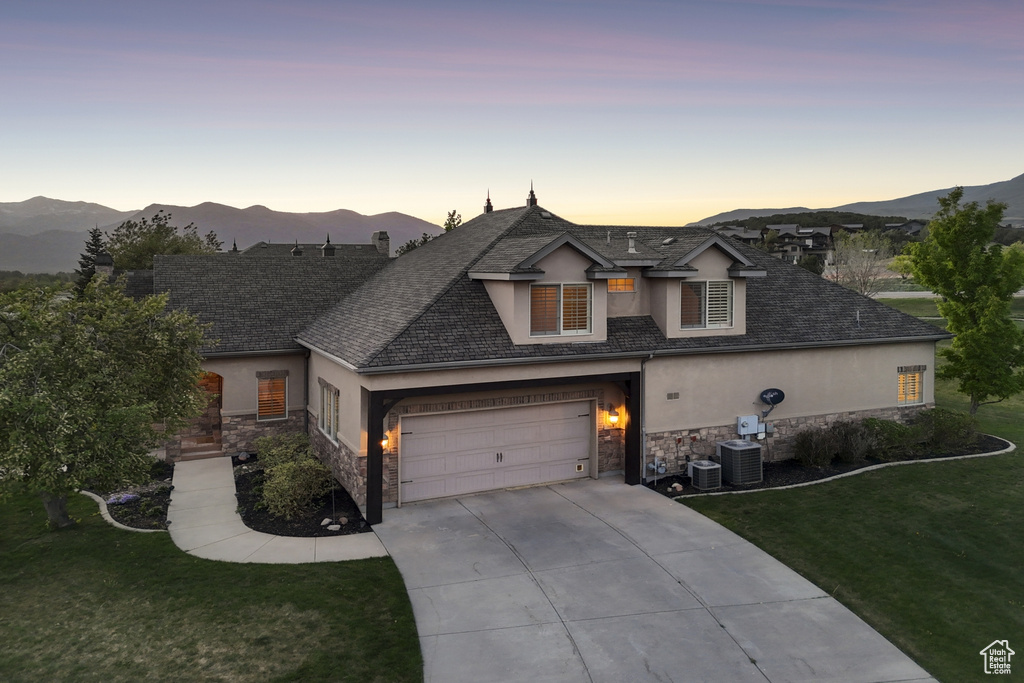 View of front of house featuring stucco siding, stone siding, driveway, a front yard, and central AC unit