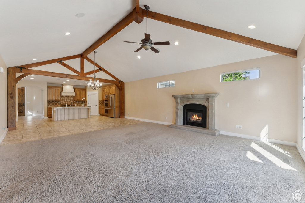 Unfurnished living room featuring beamed ceiling, a glass covered fireplace, baseboards, light carpet, and high vaulted ceiling