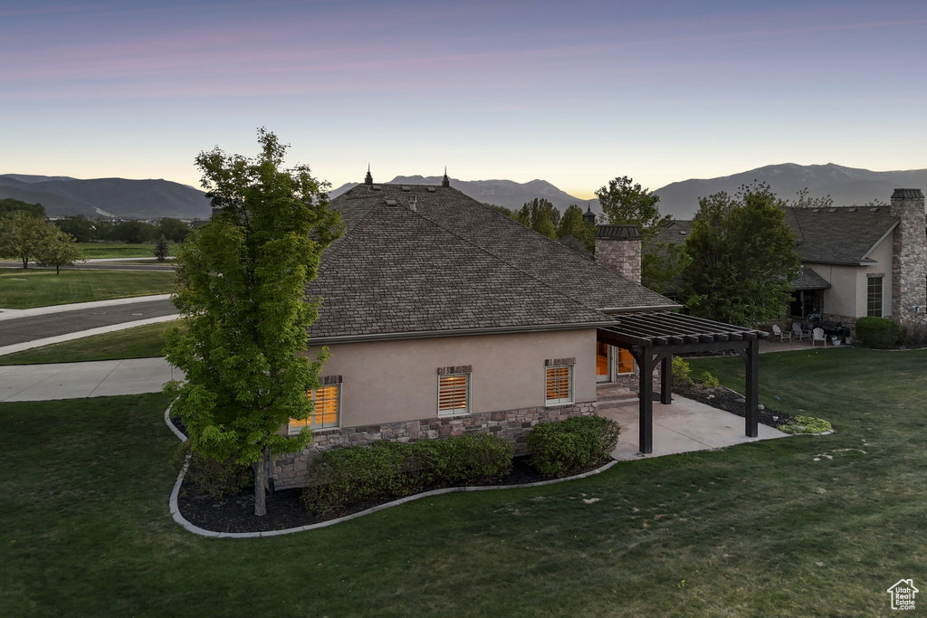 Property exterior at dusk featuring stucco siding, a pergola, a chimney, a patio, and a lawn