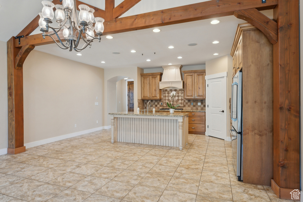 Kitchen featuring custom range hood, arched walkways, recessed lighting, decorative backsplash, and light stone counters