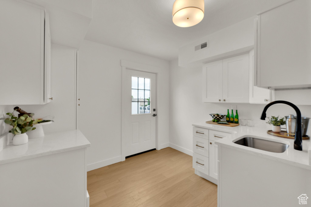 Kitchen with a sink, light wood finished floors, white cabinetry, baseboards, and light stone counters