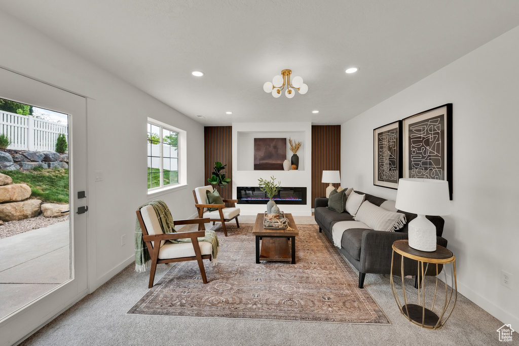 Carpeted living area with recessed lighting, baseboards, a chandelier, and a glass covered fireplace